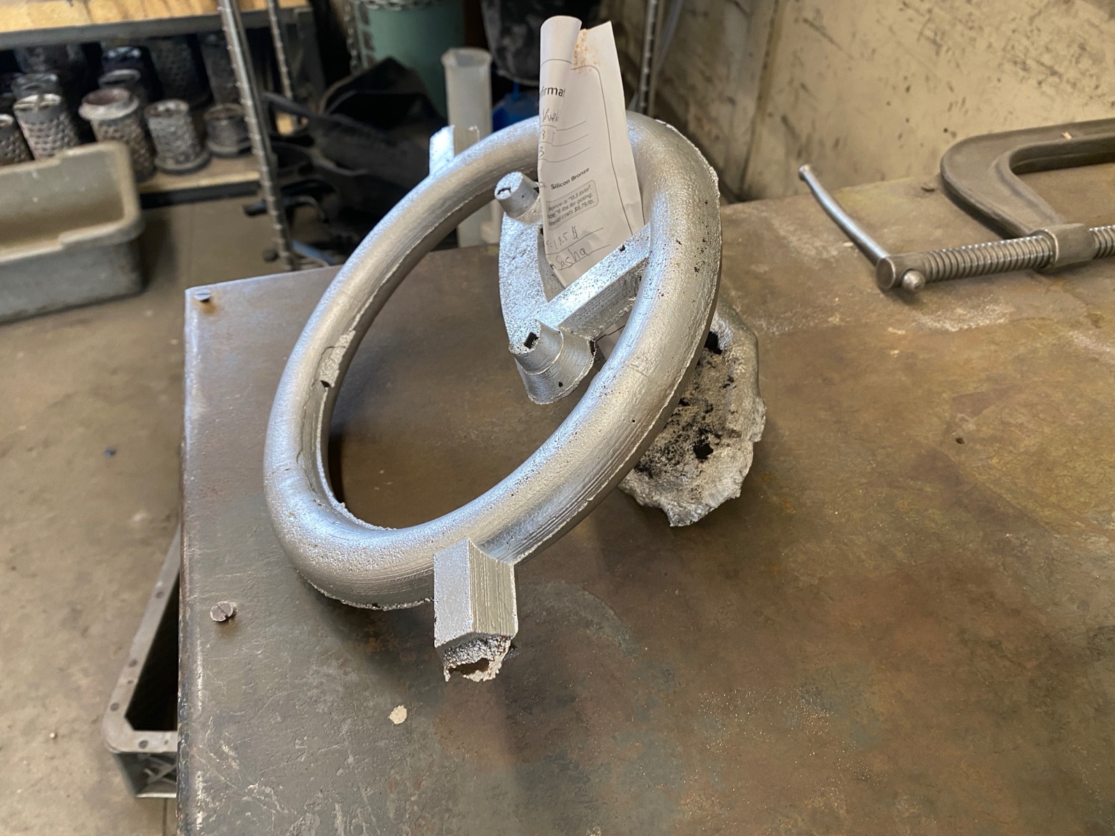 Raw aluminum casting on a steel table with the sprue, riser, and runner stubs still attached.