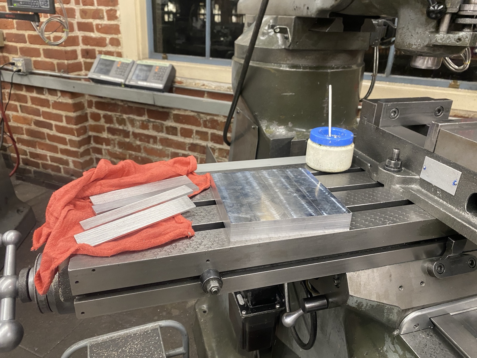 6061 aluminum block on the mill bed with milled leg blanks resting on a red rag beside it.