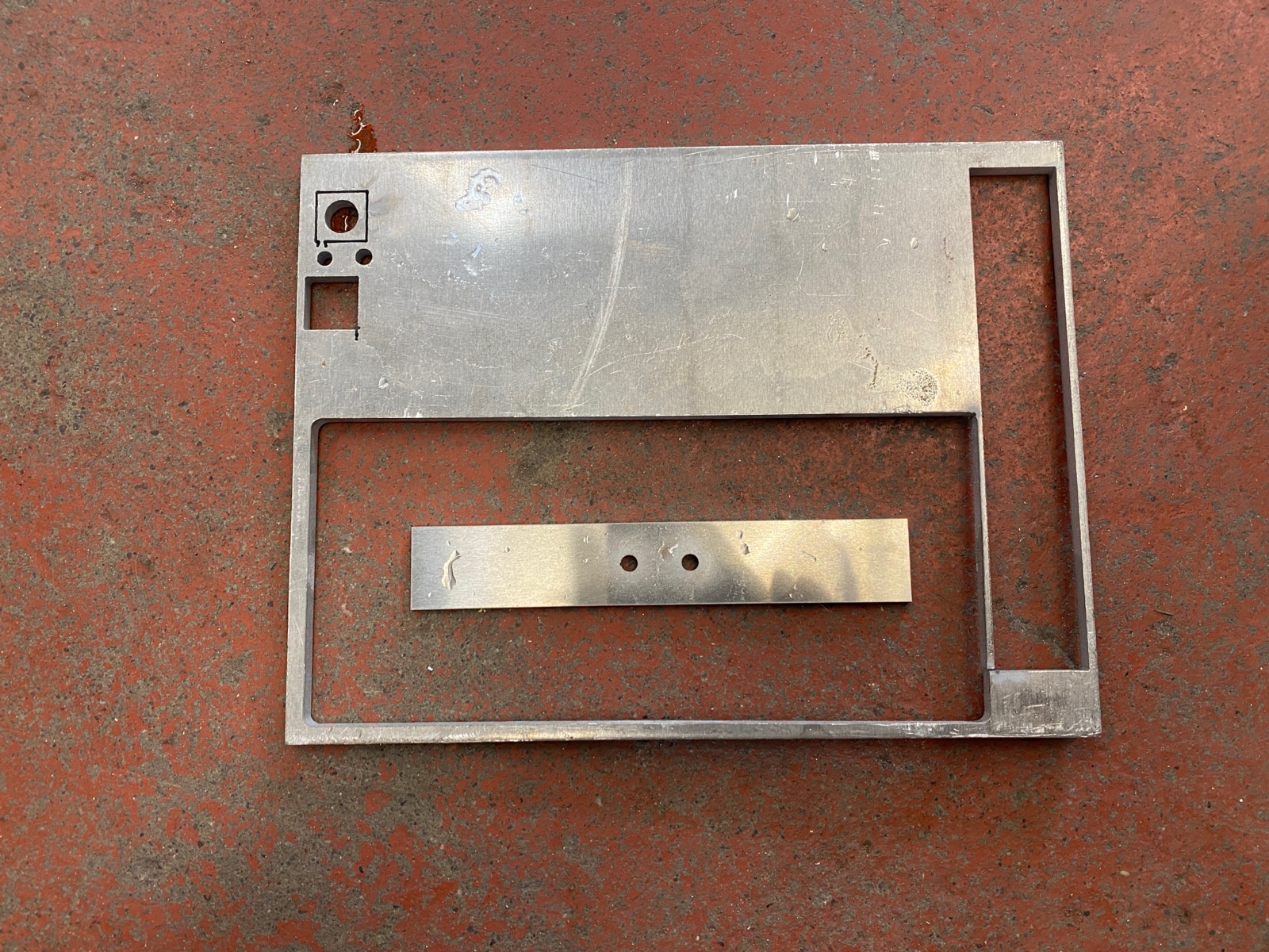 Water-jet-cut sheet metal showing the baseplate negative space and a finished baseplate piece beside it.