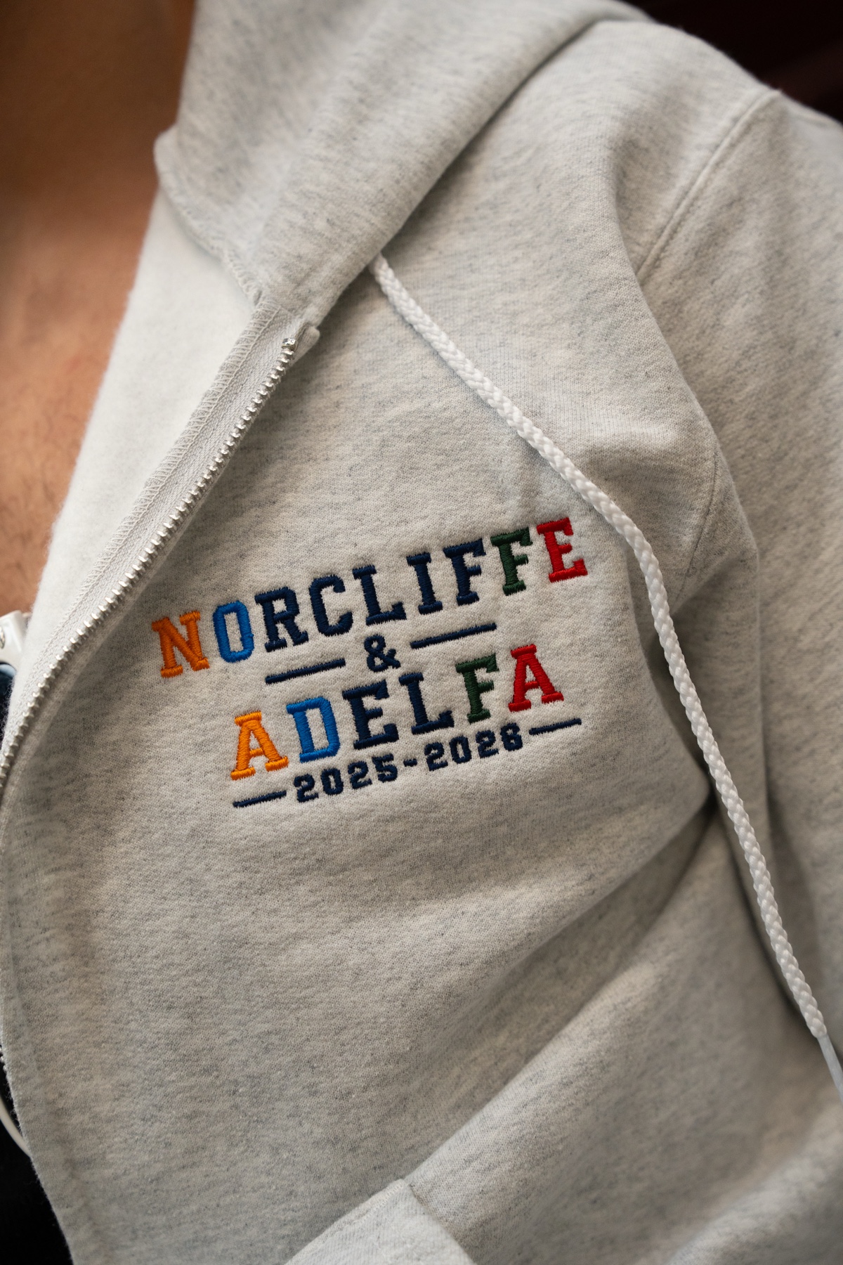 Close-up of the embroidered NORCLIFFE & ADELFA wordmark with four letters in each name colored for the four elements